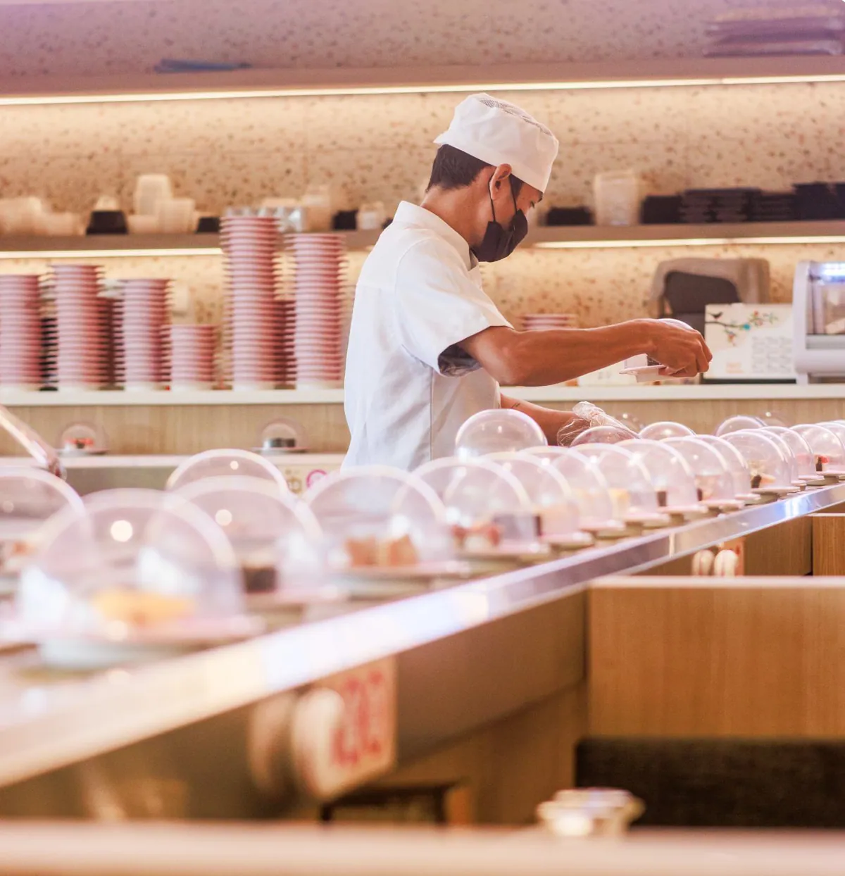 A Sushi Hiro chef placing fresh plates on the kaiten belt